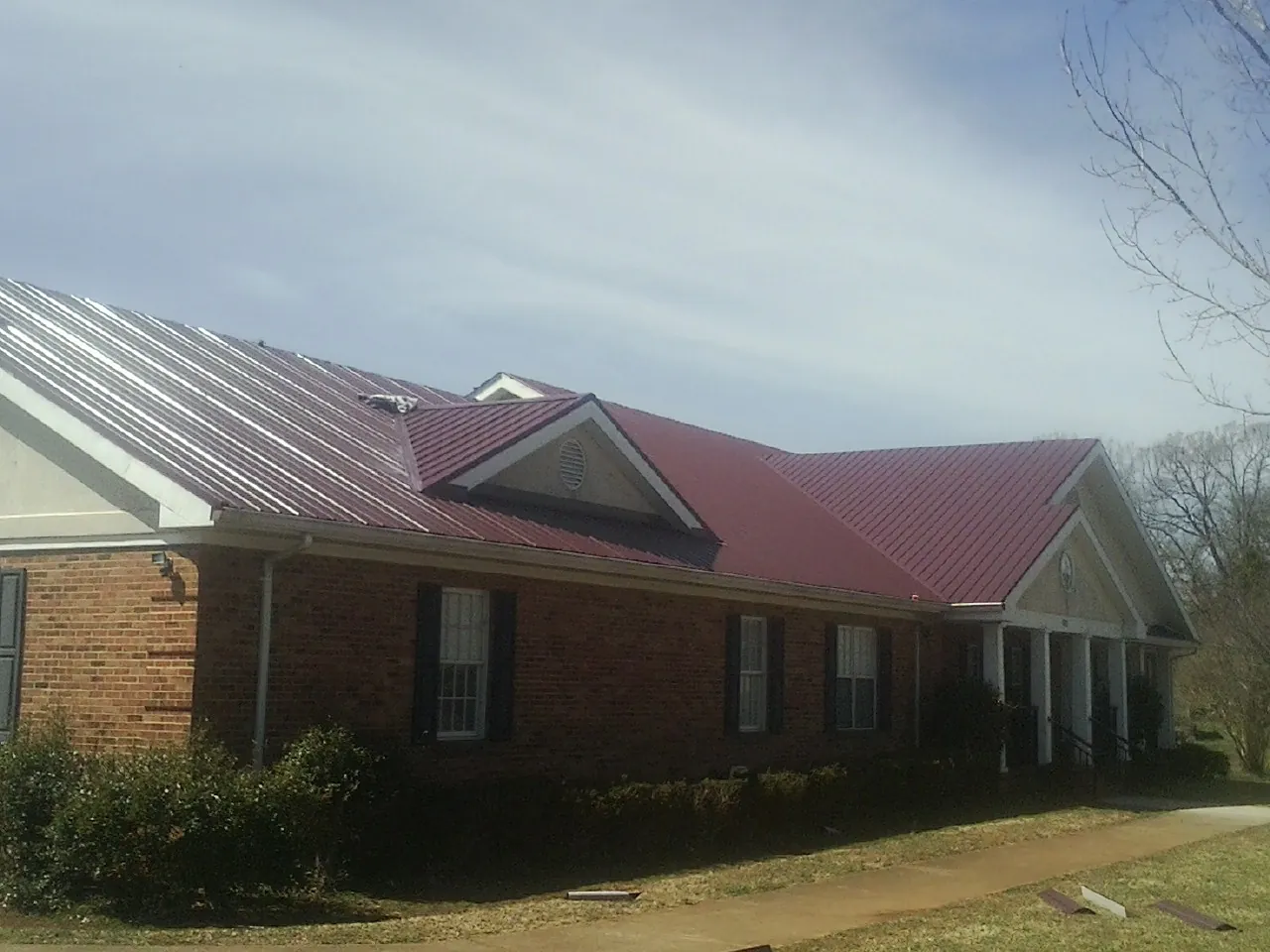 Red metal roof with gabled entries on a long brick building, from a Hail Damage Roof Repair job in Los Molinos