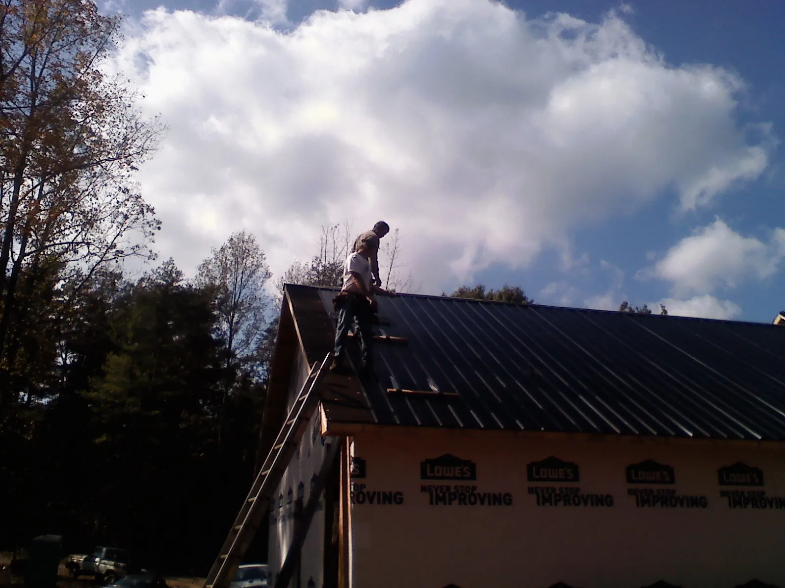 Roofer fastening dark metal panels high against a cloudy sky, from a Roof Inspection job in Los Molinos