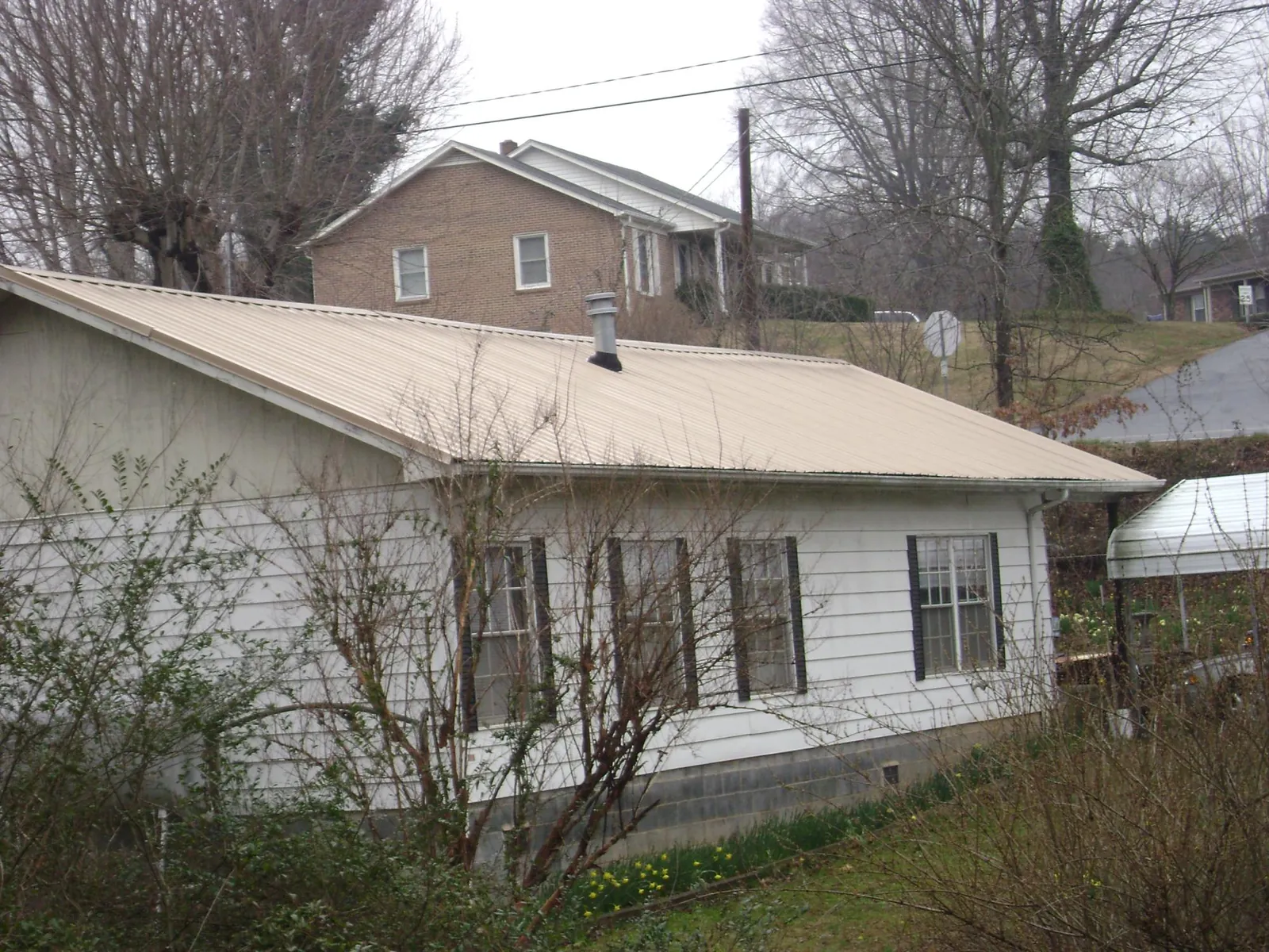 Tan metal roof on a white sided house set into a hillside — Commercial Roofing by Roofing Brothers in Los Molinos