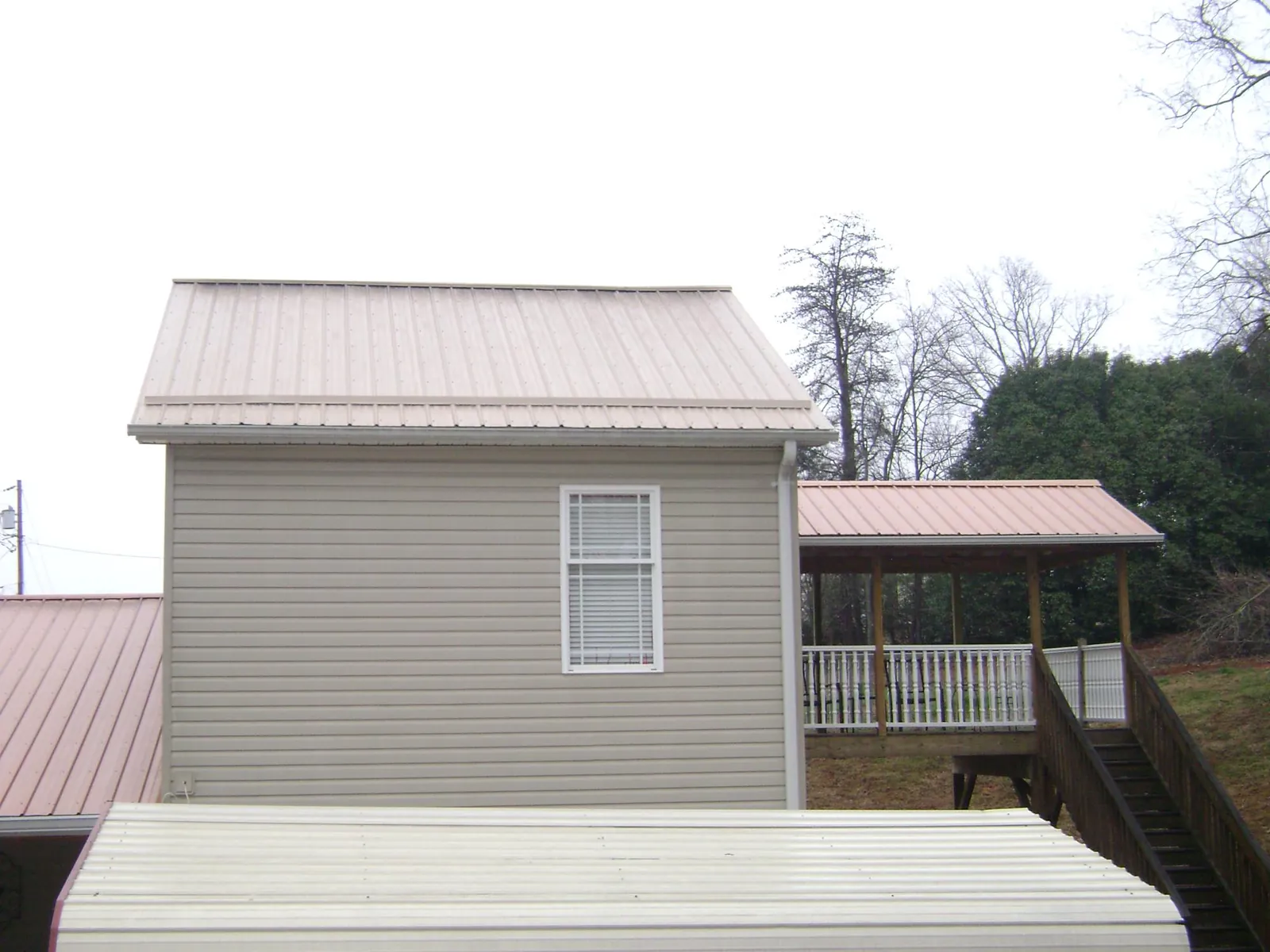Tan metal roofs on a two story addition and attached porch, from a Roof Replacement job in Los Molinos
